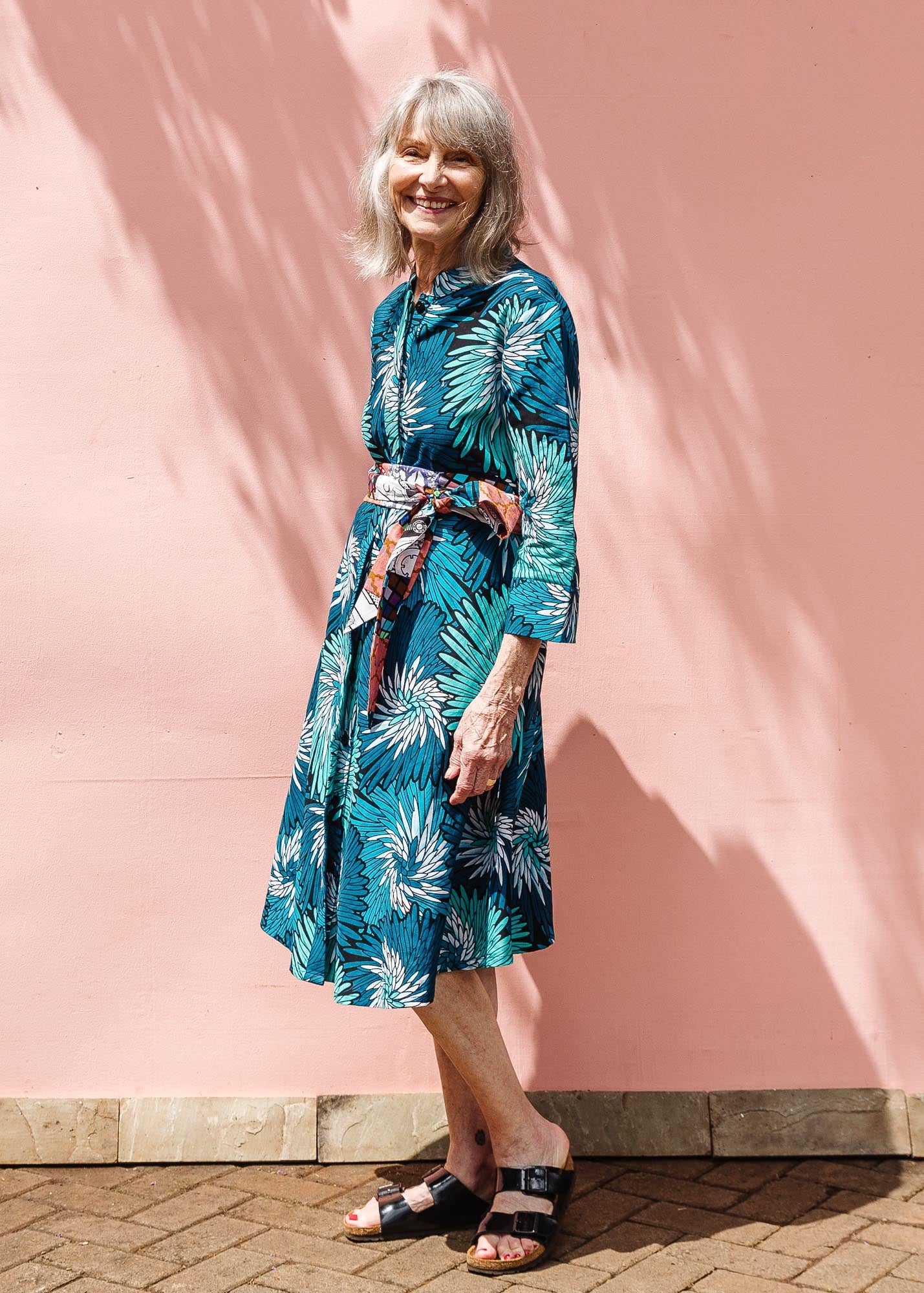 The model is wearing turquoise, black, pacific blue, slate and white feathered spiral print dress