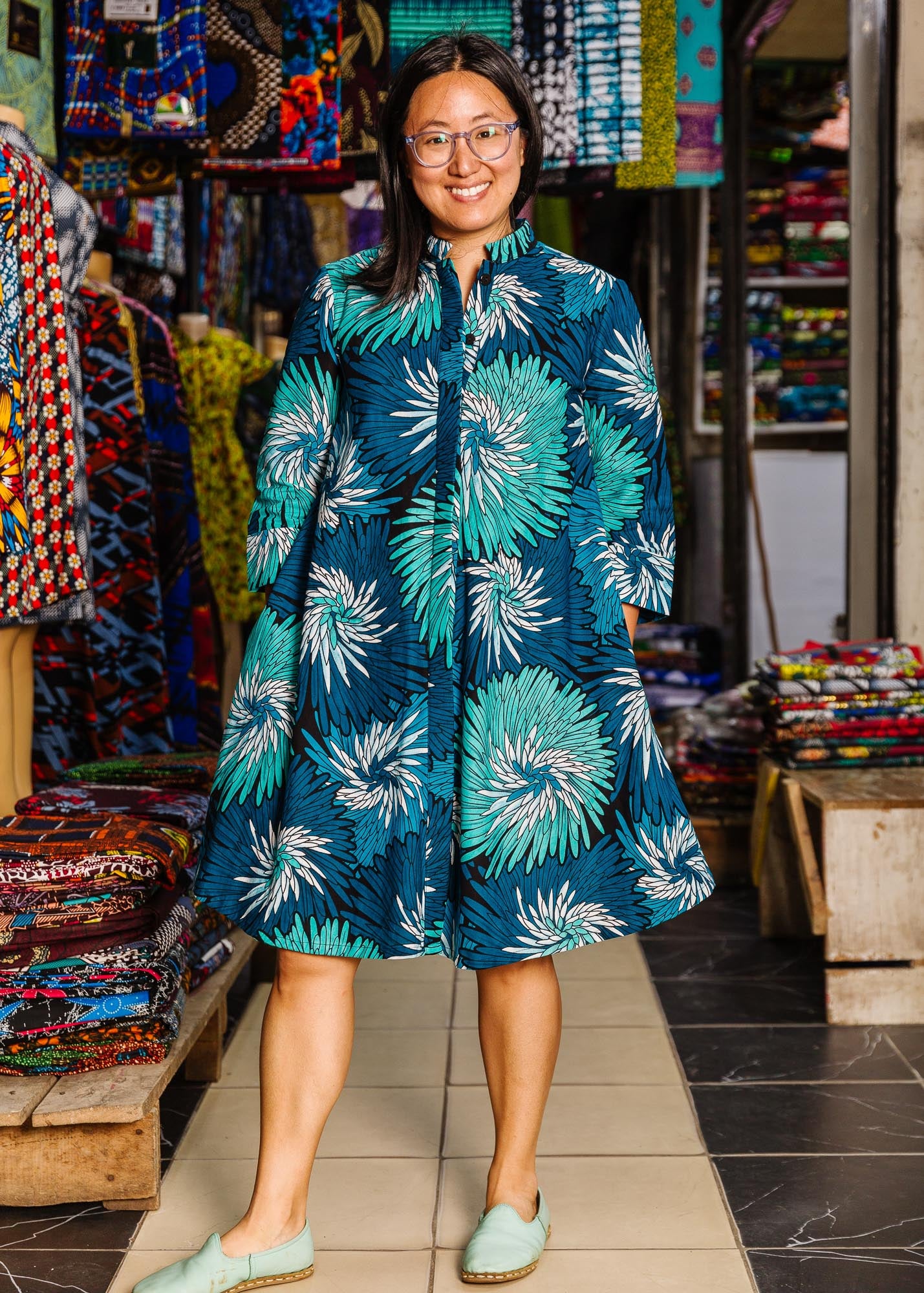 The model is wearing turquoise, black, pacific blue, slate and white feathered spiral print dress