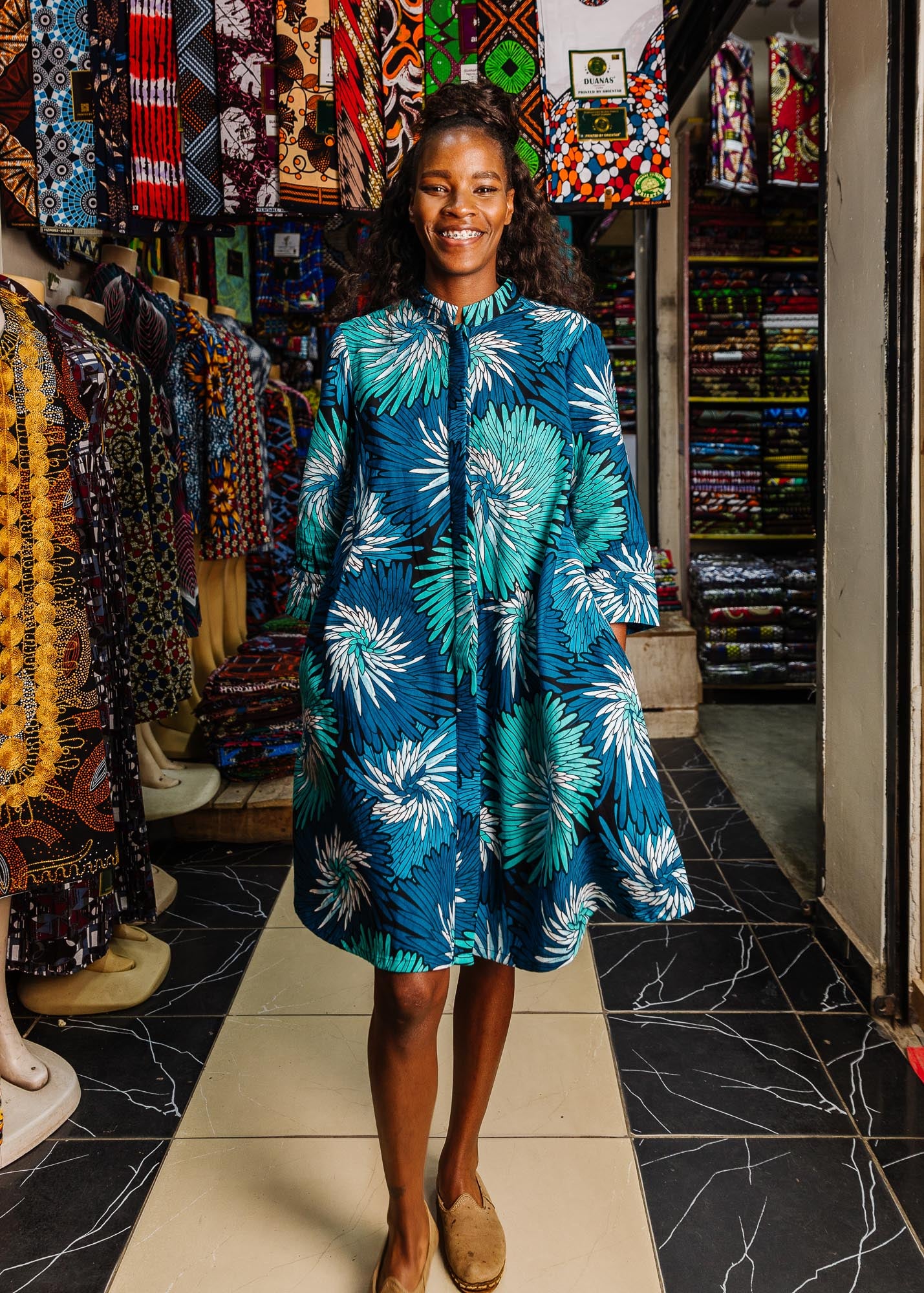 The model is wearing turquoise, black, pacific blue, slate and white feathered spiral print dress