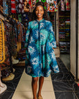 The model is wearing turquoise, black, pacific blue, slate and white feathered spiral print dress