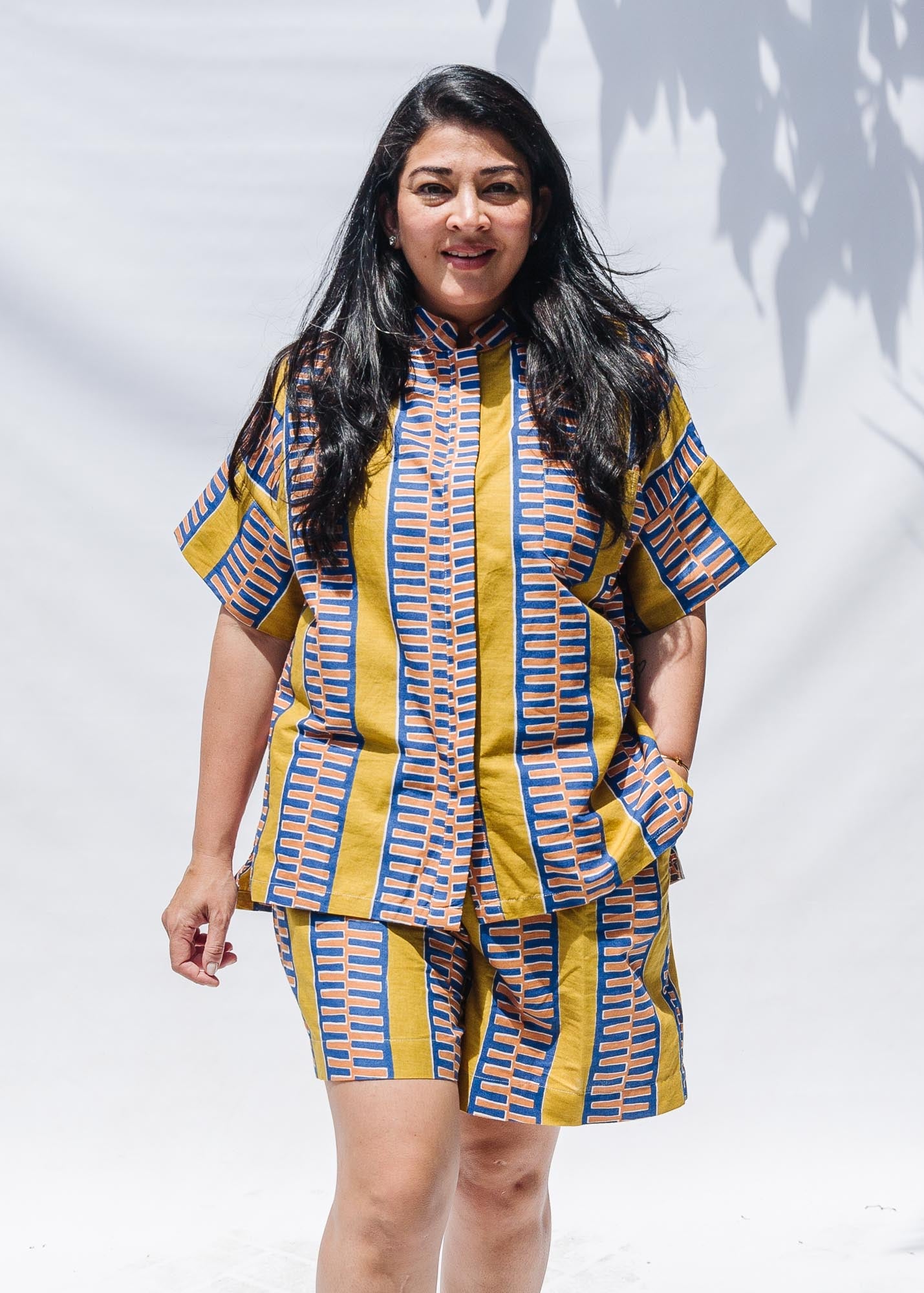 The model is wearing olive-yellow, blue, orange and white geometric printed shirt