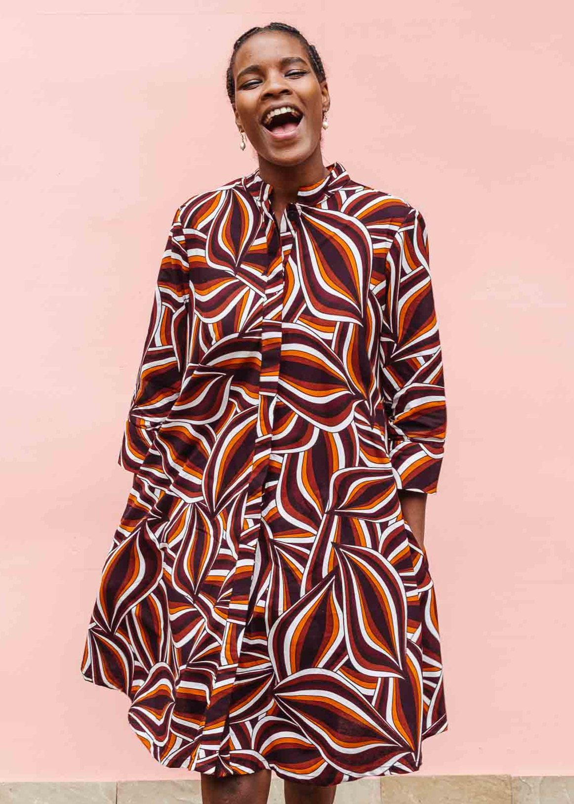 Model wearing brown, orange, burgundy and white abstract print dress.