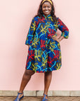 The model is wearing blue, red, yellow, black and aqua vine print dress