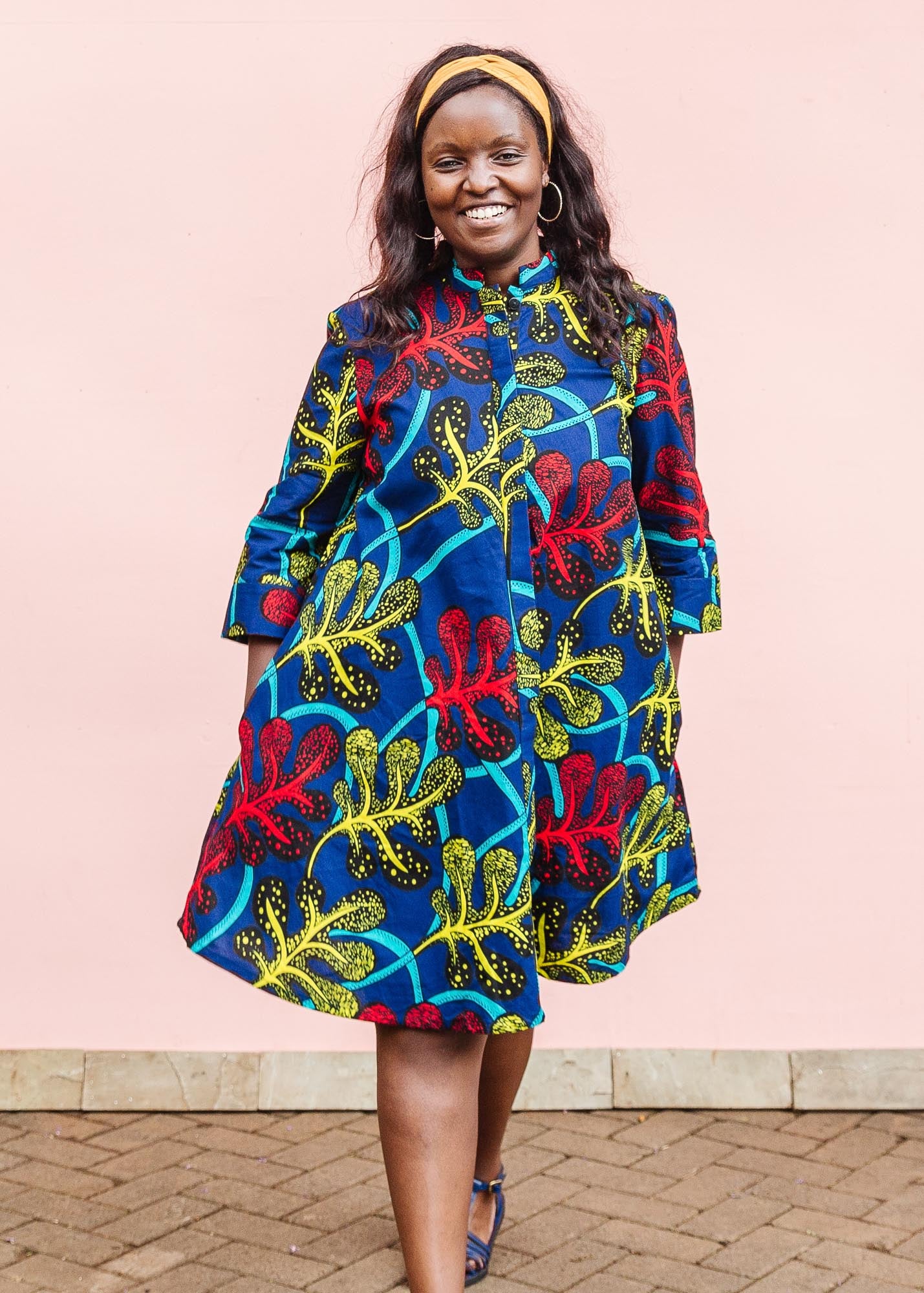 The model is wearing blue, red, yellow, black and aqua vine print dress