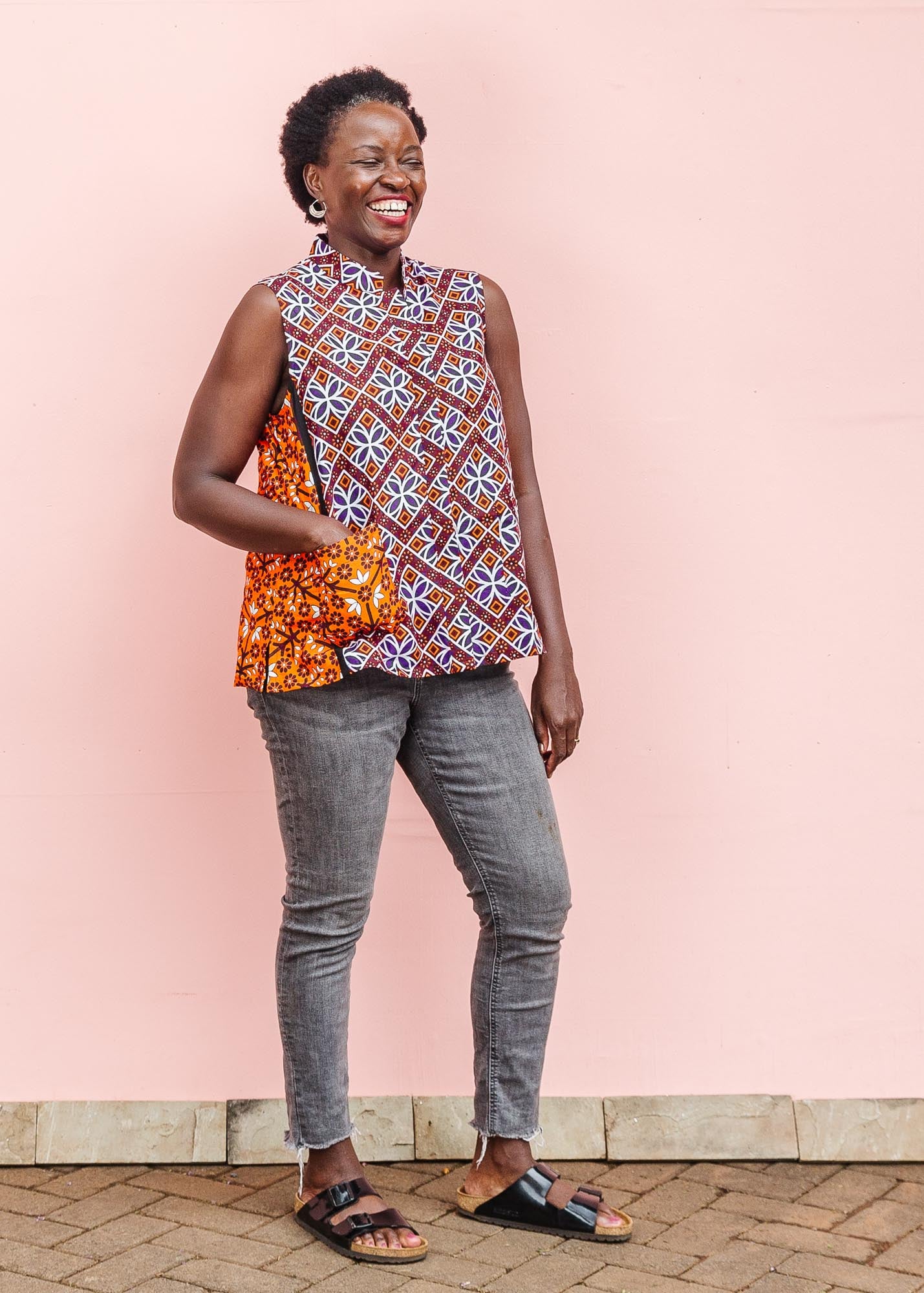 The model is wearing  orange, purple, white and black mixed pattern kanga tank