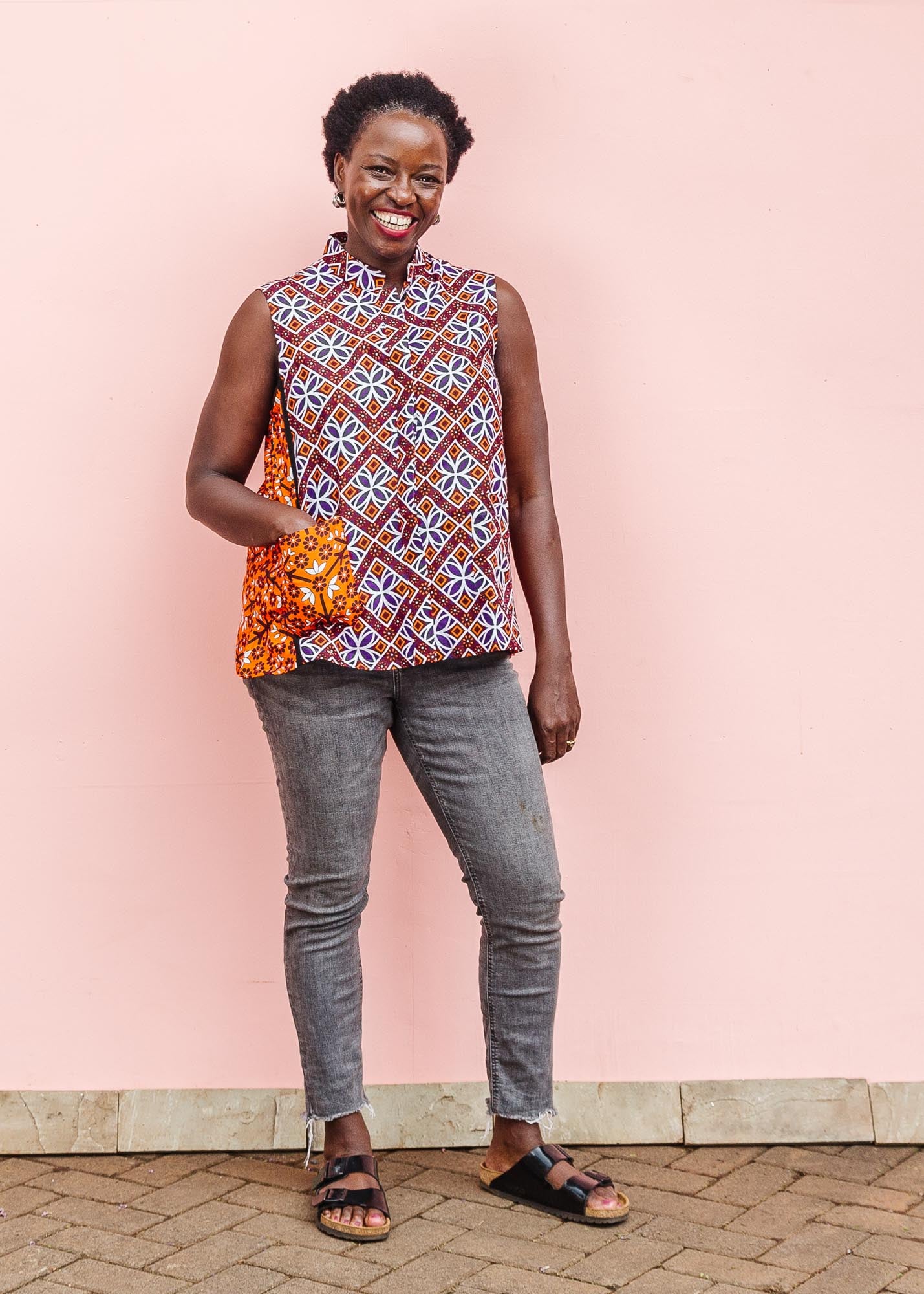 The model is wearing  orange, purple, white and black mixed pattern kanga tank