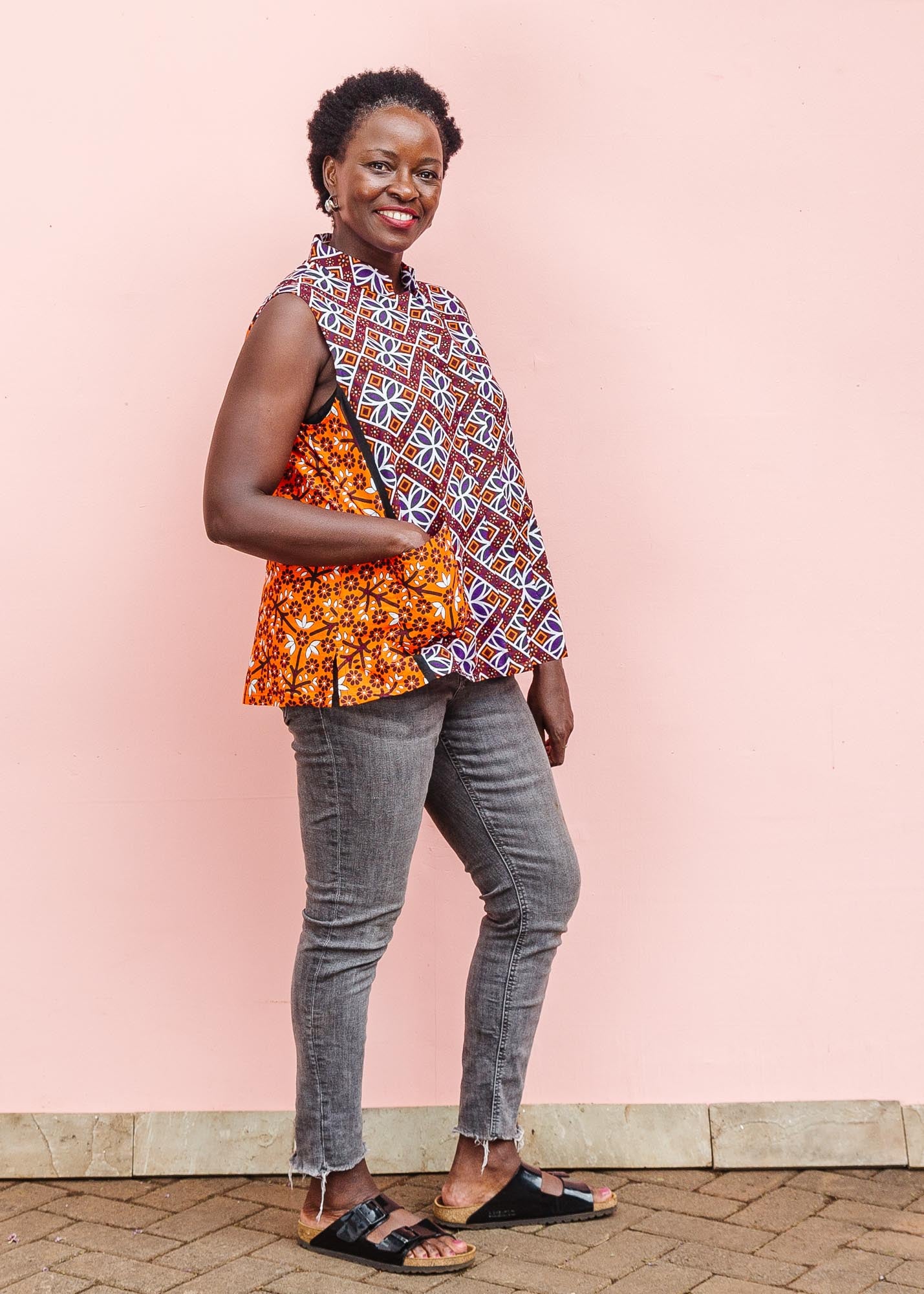 The model is wearing  orange, purple, white and black mixed pattern kanga tank