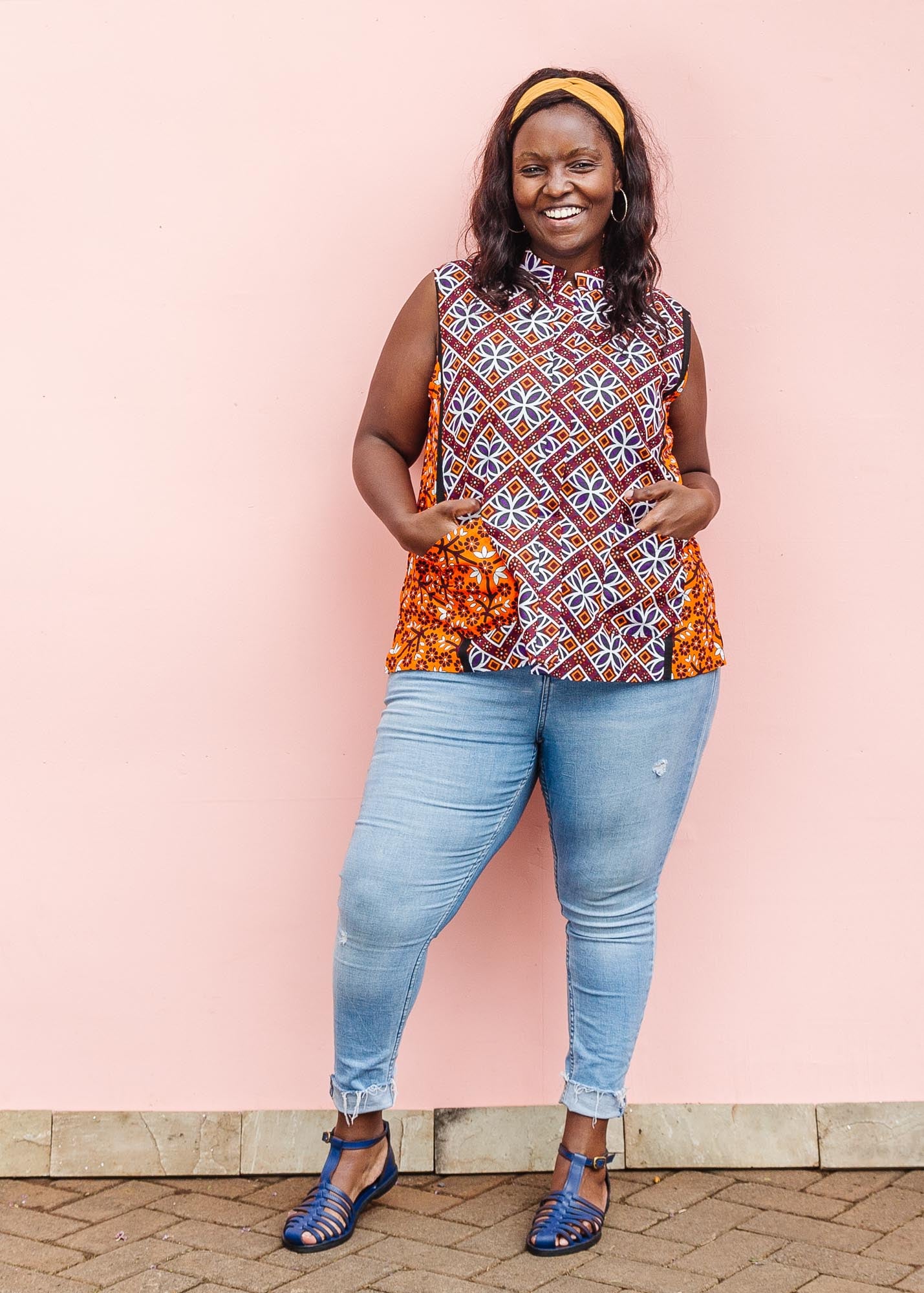 The model is wearing  orange, purple, white and black mixed pattern kanga tank