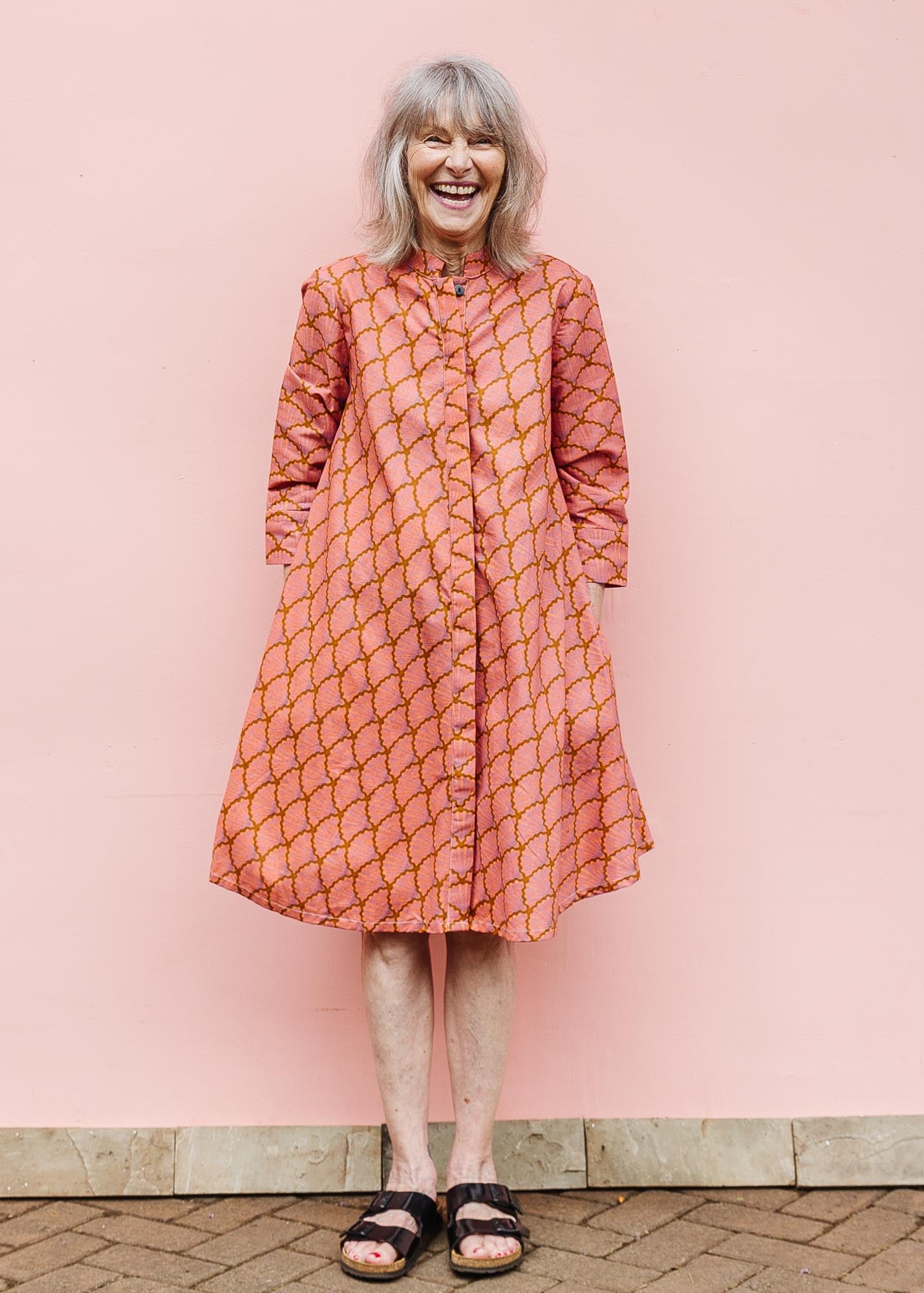 The model is wearing peach-pink, lavender and brown seashell print dress