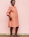 The model is wearing peach-pink, lavender and brown seashell print dress