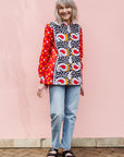 The model is wearing red, white, black and orange mixed pattern long sleeved kanga shirt