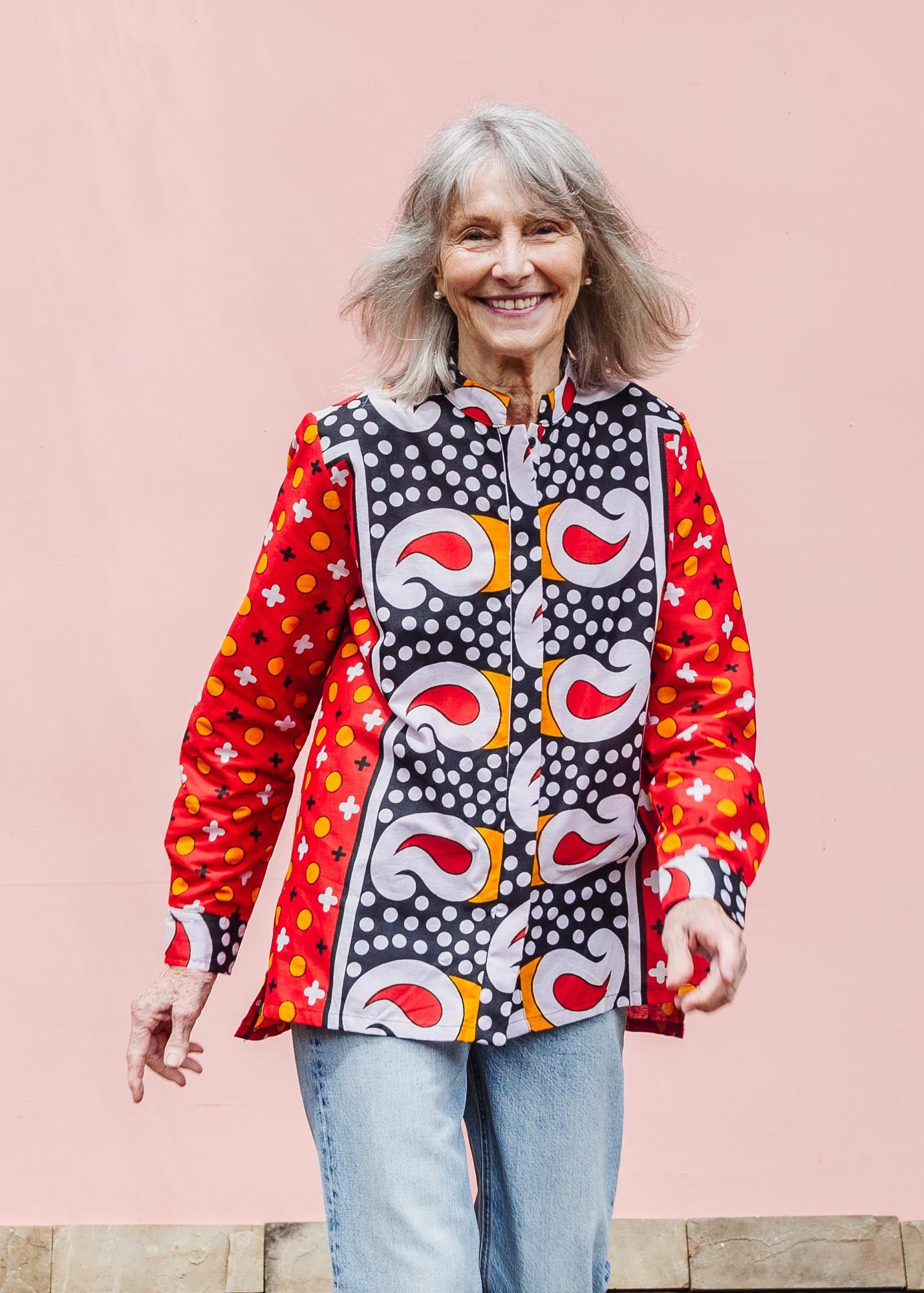 The model is wearing red, white, black and orange mixed pattern long sleeved kanga shirt