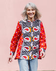 The model is wearing red, white, black and orange mixed pattern long sleeved kanga shirt