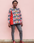 The model is wearing red, white, black and orange mixed pattern long sleeved kanga shirt