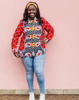 The model is wearing red, white, black and orange mixed pattern long sleeved kanga shirt