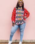 The model is wearing red, white, black and orange mixed pattern long sleeved kanga shirt