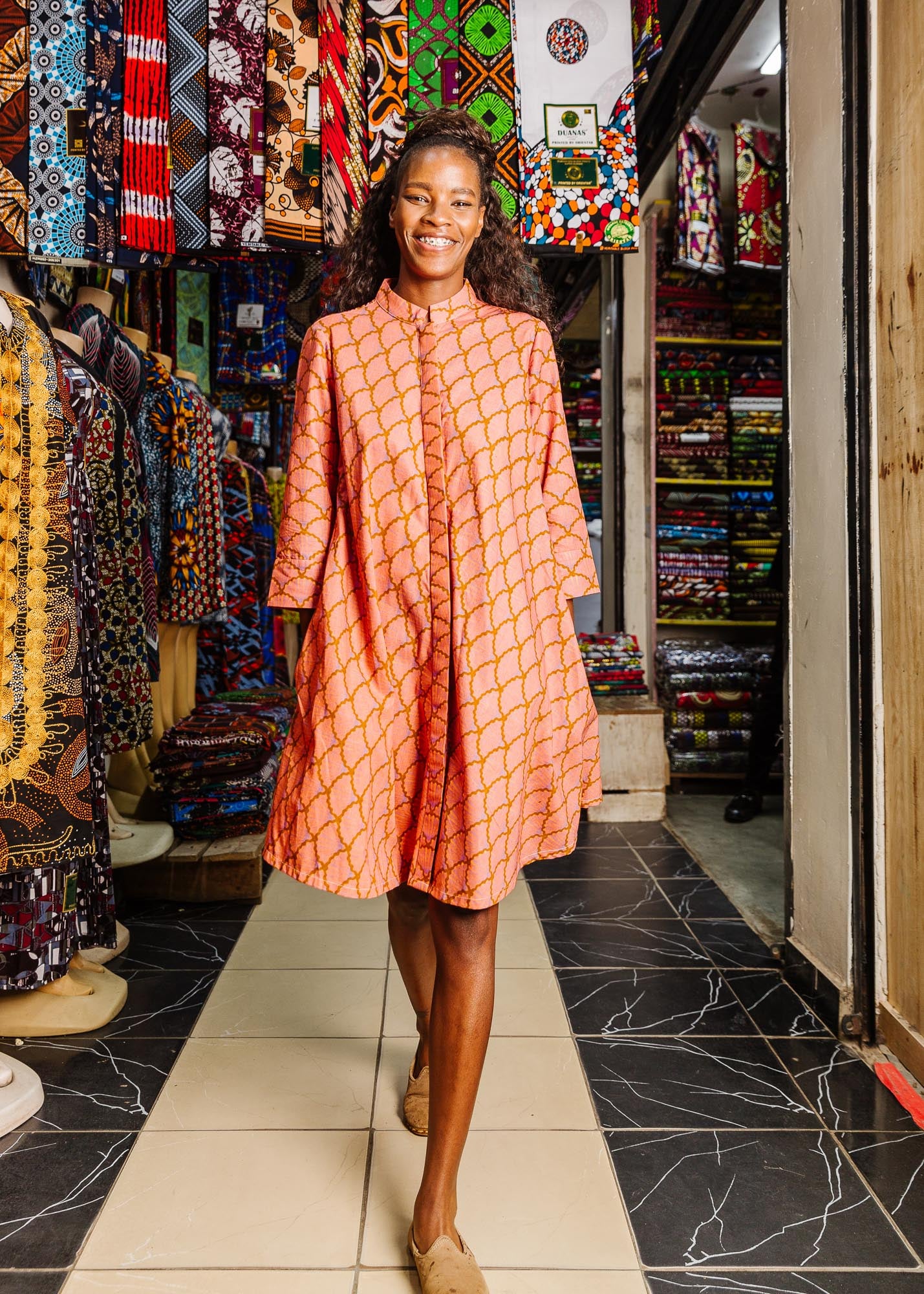 The model is wearing peach-pink, lavender and brown seashell print dress