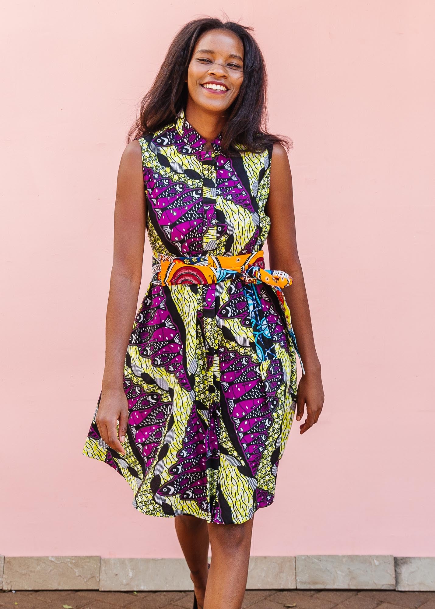 The model is wearing yellow-green dress with purple, black, white fish print 