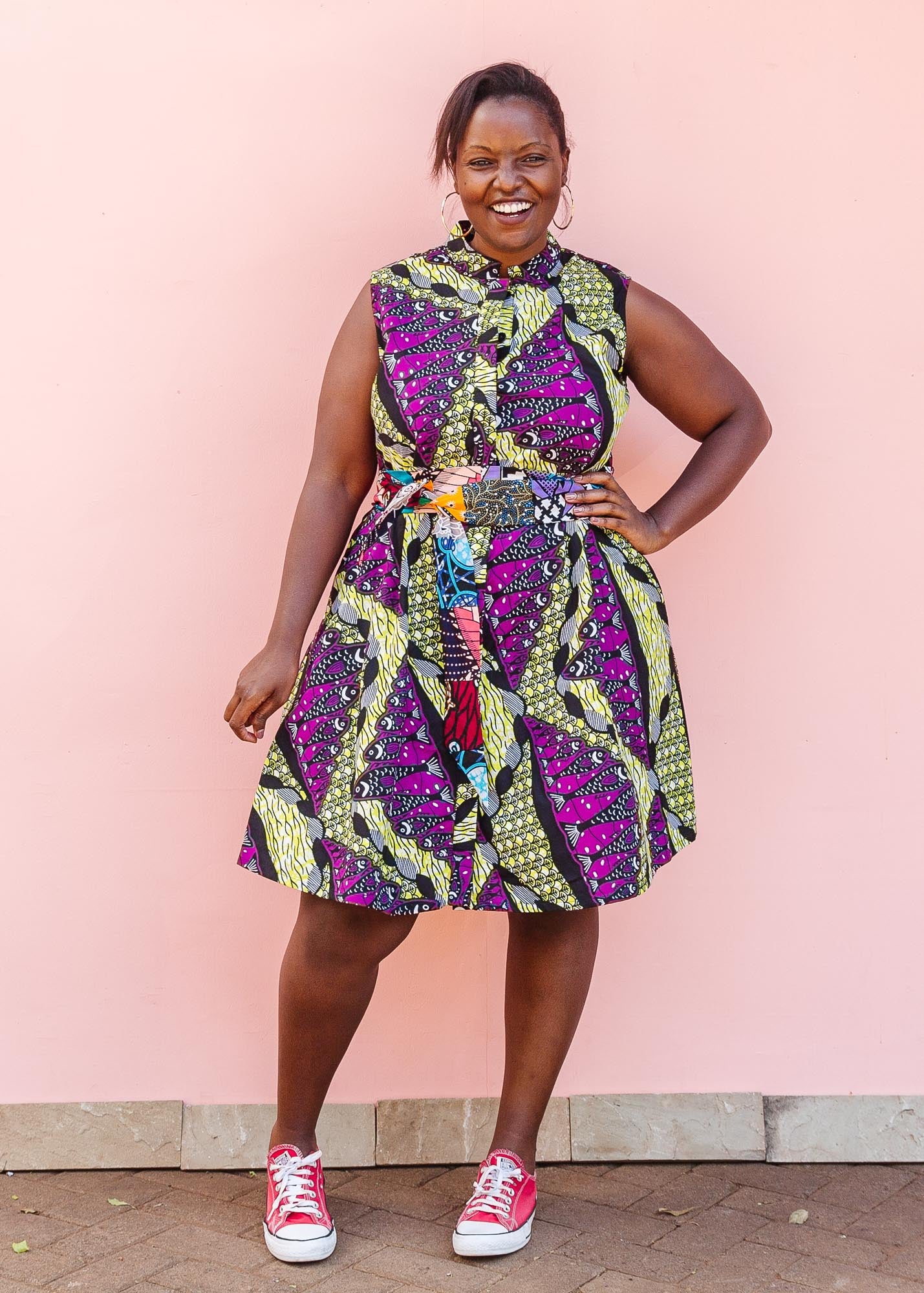 The model is wearing yellow-green dress with purple, black, white fish print 