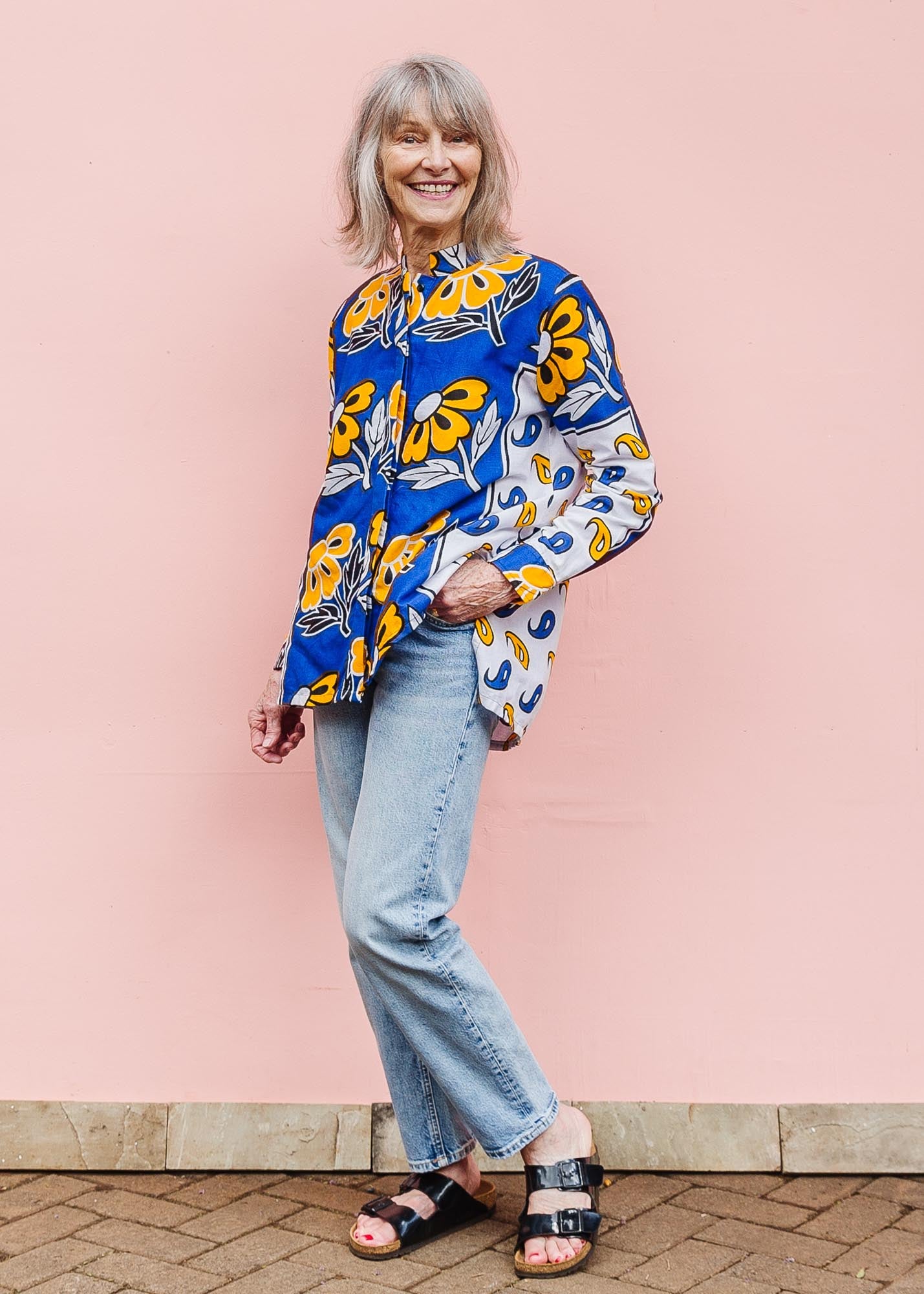 The model is wearing white, blue, black and orange mixed pattern long sleeved kanga shirt