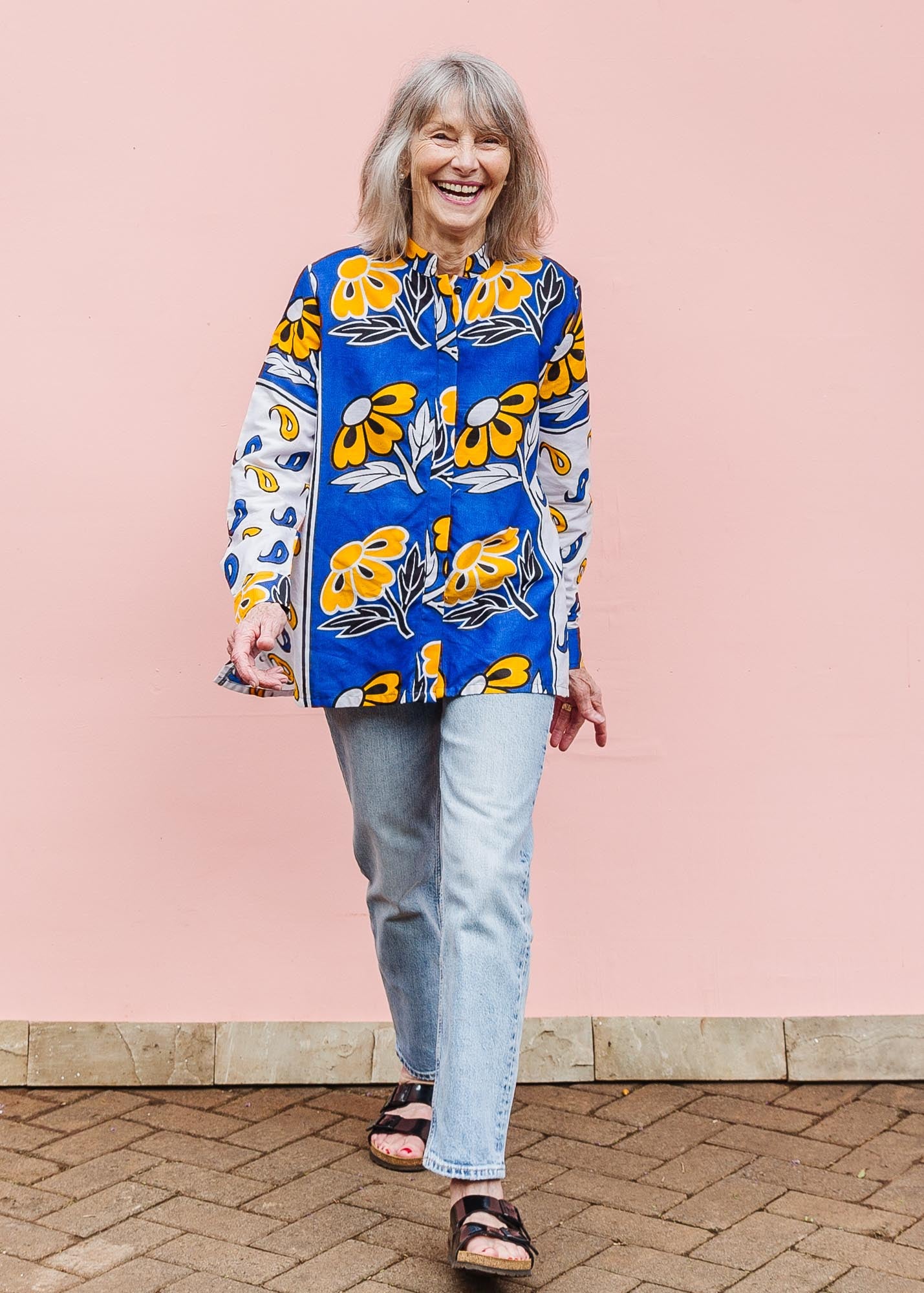 The model is wearing white, blue, black and orange mixed pattern long sleeved kanga shirt