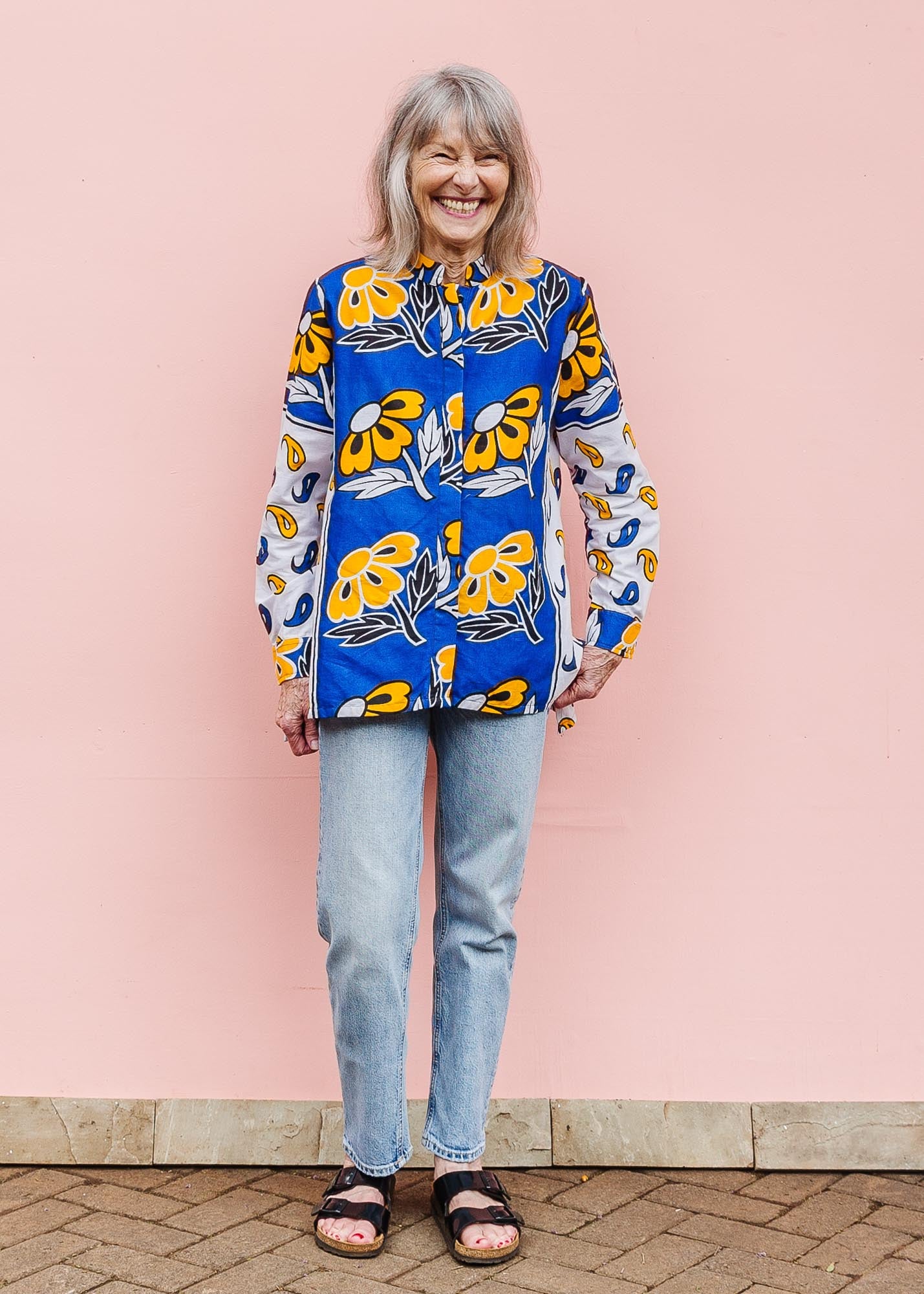 The model is wearing white, blue, black and orange mixed pattern long sleeved kanga shirt