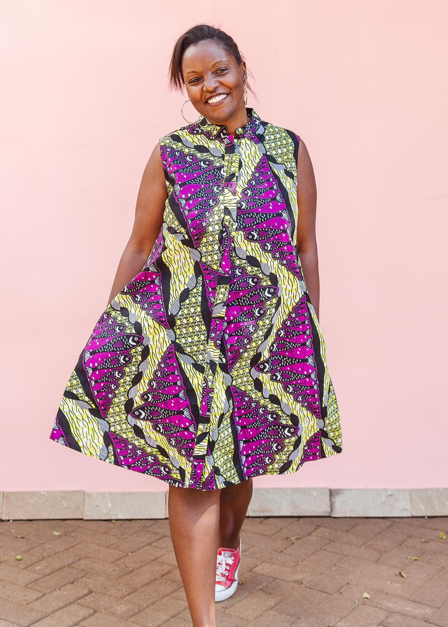 The model is wearing yellow-green dress with purple, black, white fish print 