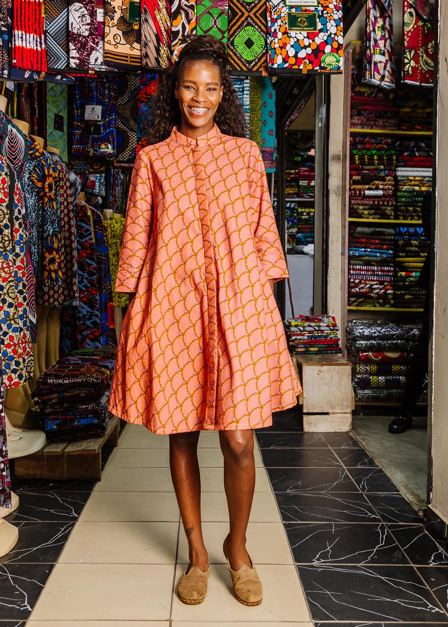 The model is wearing peach-pink, lavender and brown seashell print dress